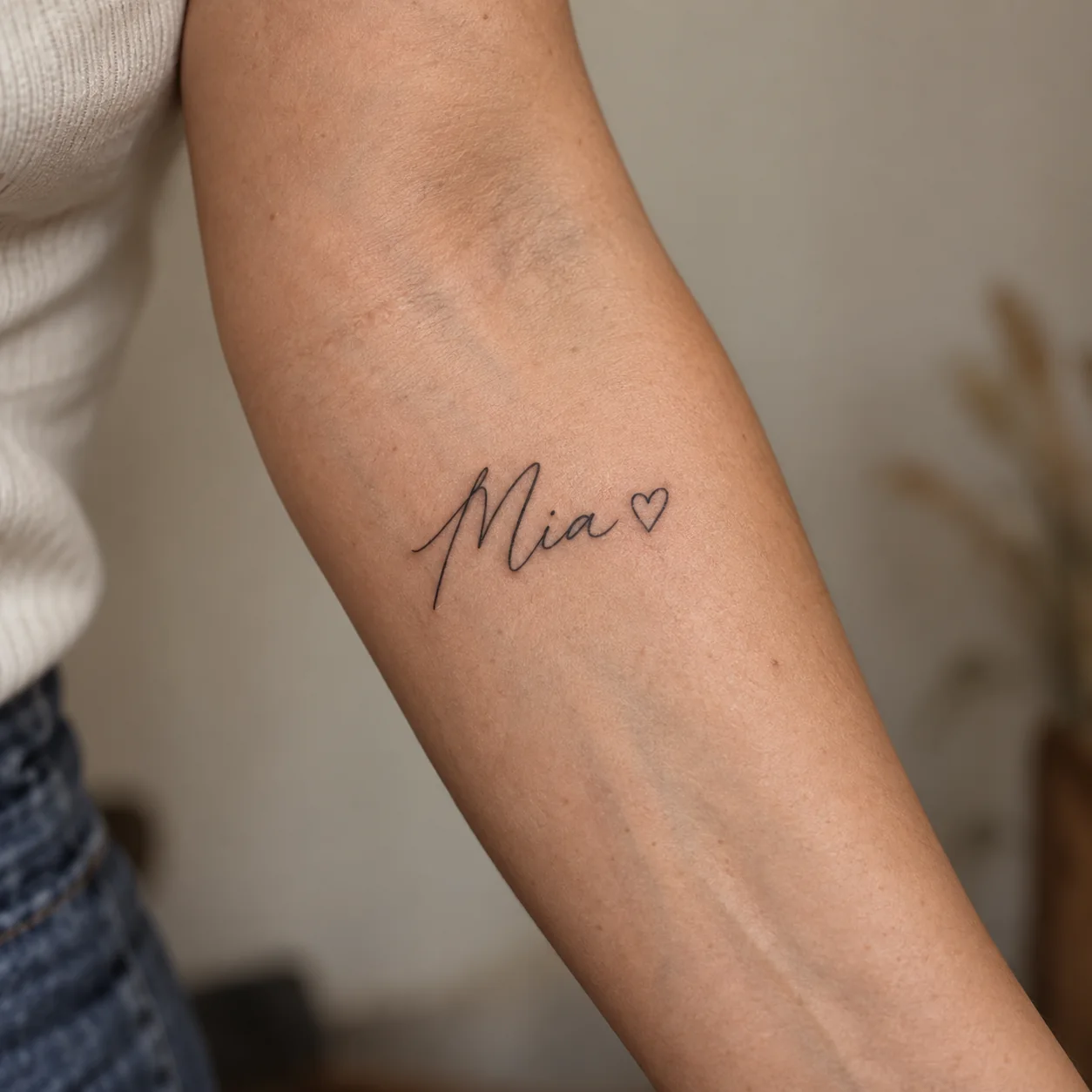 Bozza di tatuaggio con il nome Mia in linee sottili e un piccolo cuore contornato sull’interno dell’avambraccio di una persona adulta