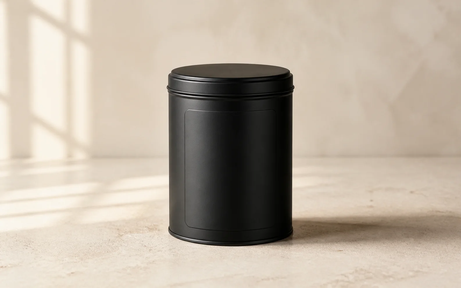 Matte black coffee tin on pale limestone with a blank label panel